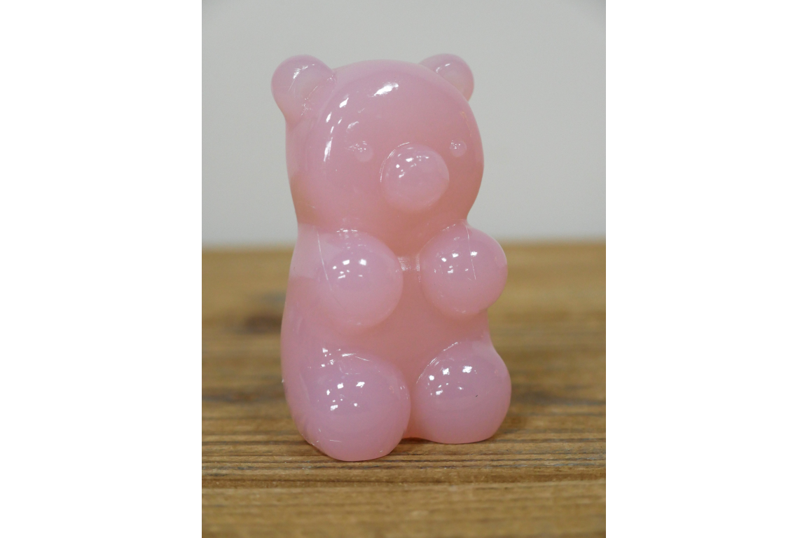 Pink gummy bear-shaped object on a wooden surface with a white background