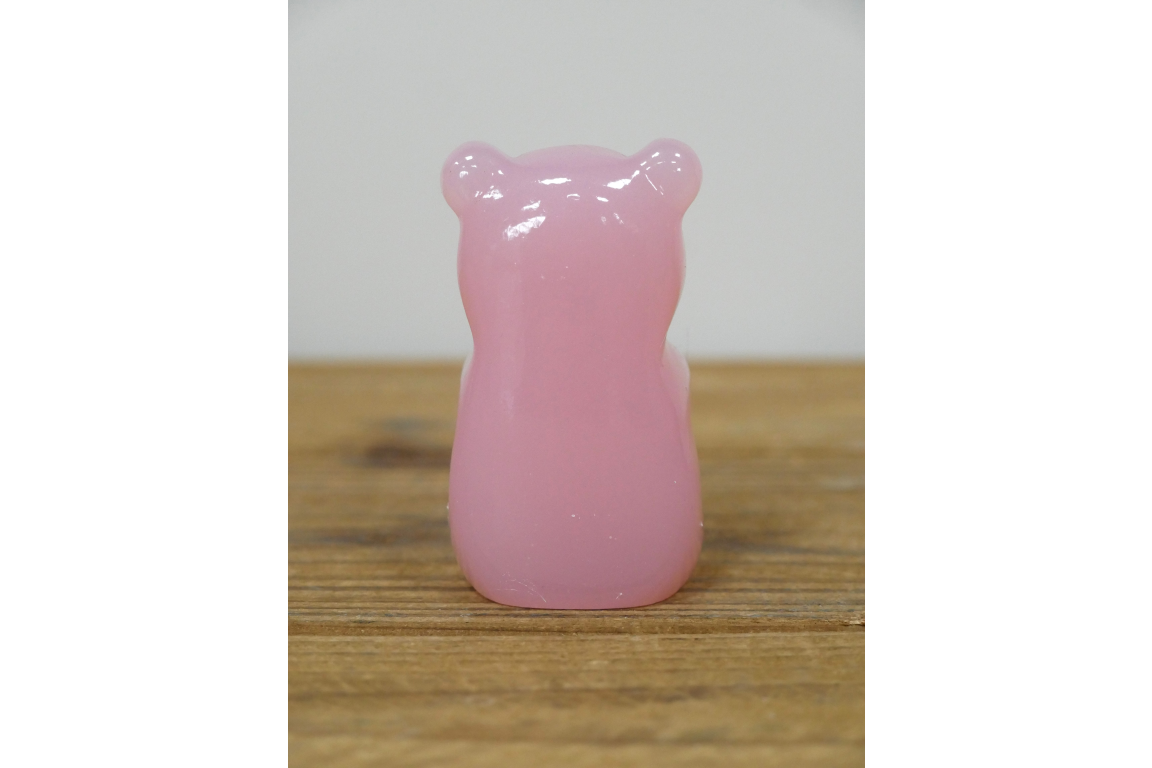 Pink bear-shaped object on a wooden surface with a white background